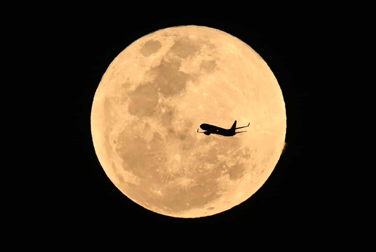 A silhouette of an aircraft, with a bright large yellow moon behind it.