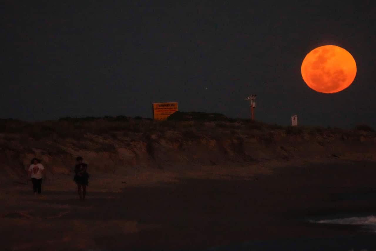 A supermoon rising above the hills of a beach.