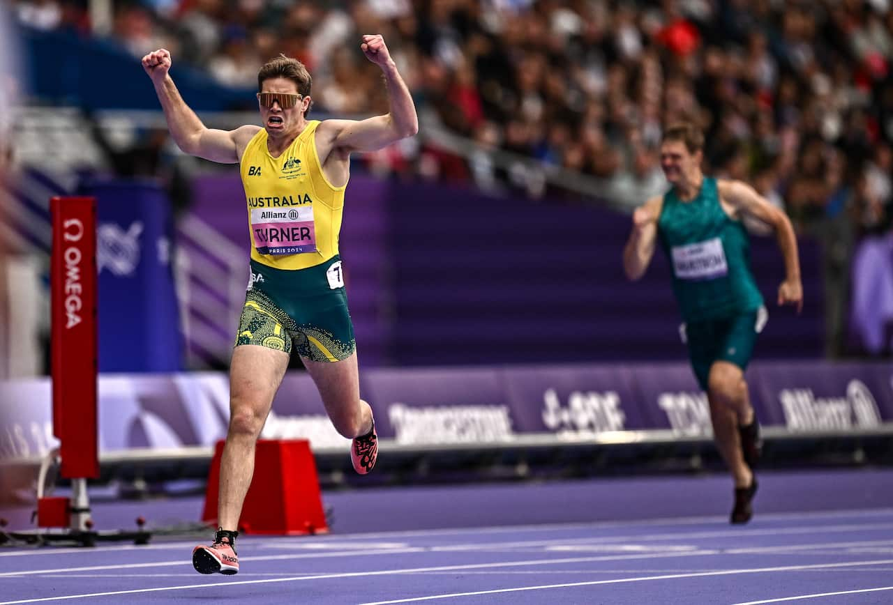 A sprinter in an Australian green and old uniform running. Another sprinter can be seen behind him.