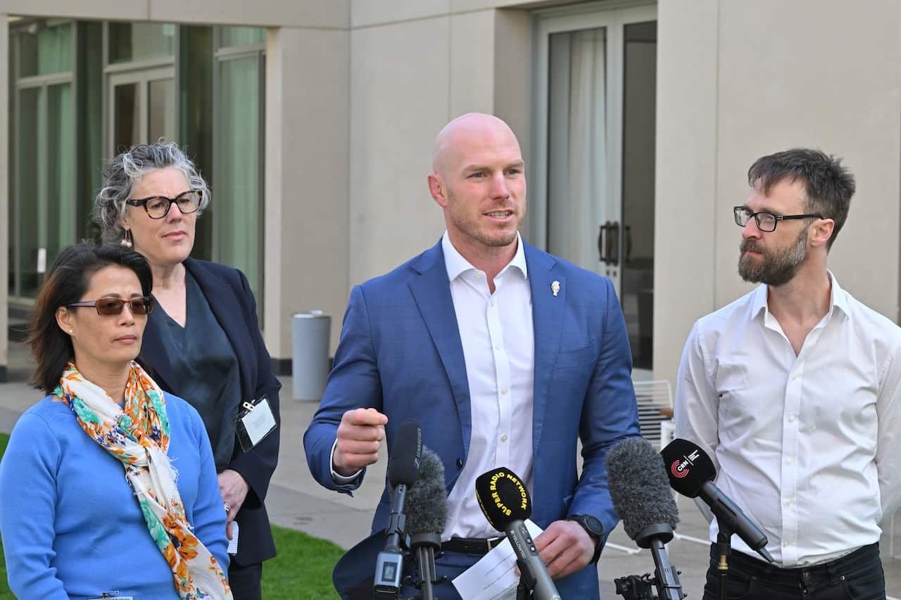 Four people - two men and two women - stand in front of media microphones.