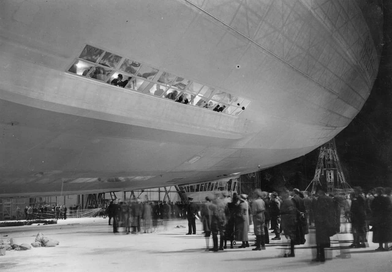 Onlookers look up at passengers in the windows of the Hindenburg airship in a hanger in the 1930s.