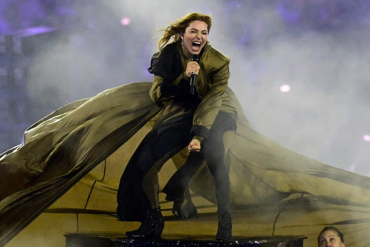 A singer wearing a flowing olive cape performs as she holds a microphone in her right hand