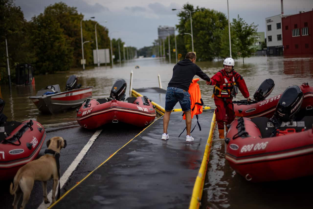 A man extends his arm to a resident, standing on a platform surrounded by red inflated lifeboats. 