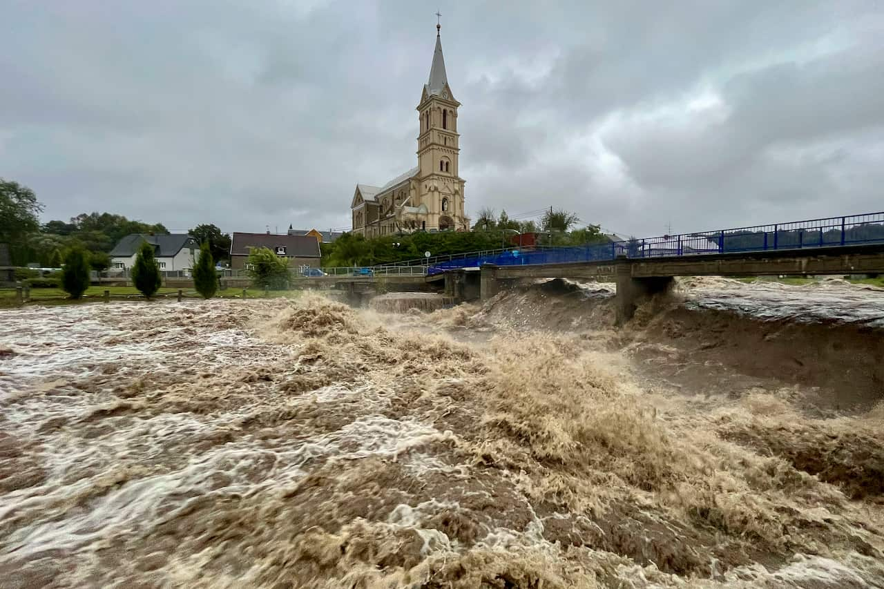 Water gushes under a bridge with a chapel in the background.