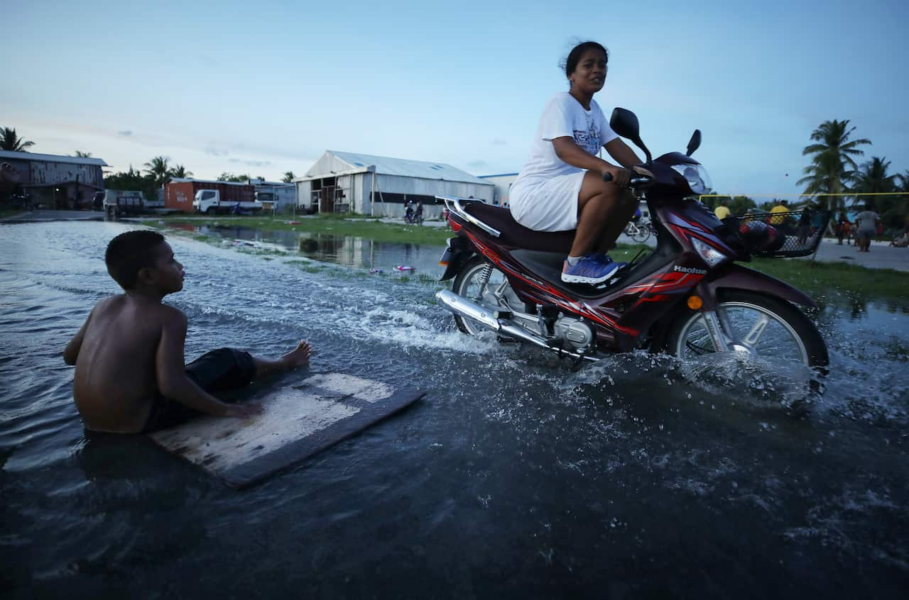 A woman rides her bike through the water as a young boy watches her.