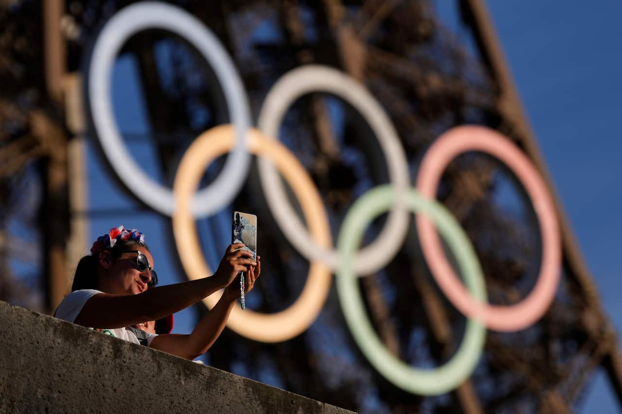 A person taking a selfie in front of the Eiffel Tower's Olympic rings.