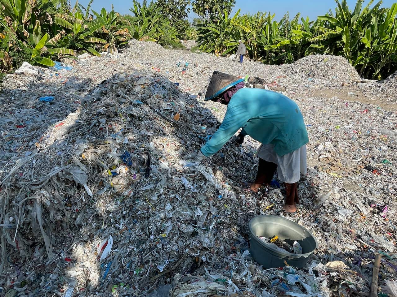 A woman sorts through a large mound of plastic and paper waste