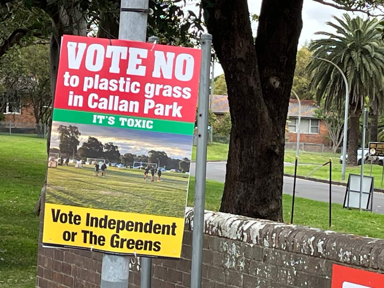 A campaign poster with large, bold text above a picture of kids playing football is displayed on a pole.