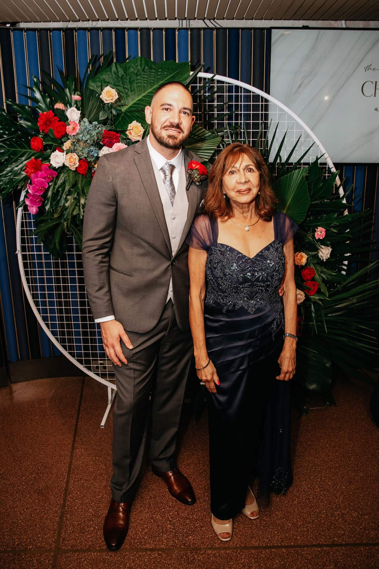 A man in a suit is standing next to an elderly woman in a dress.