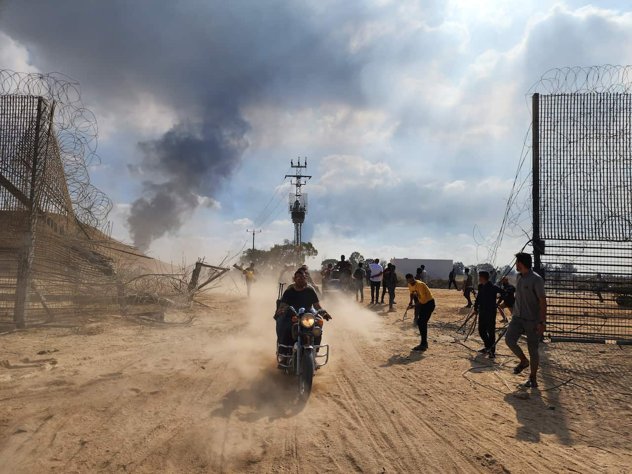 A man on a motorbike rides through a broken fence.