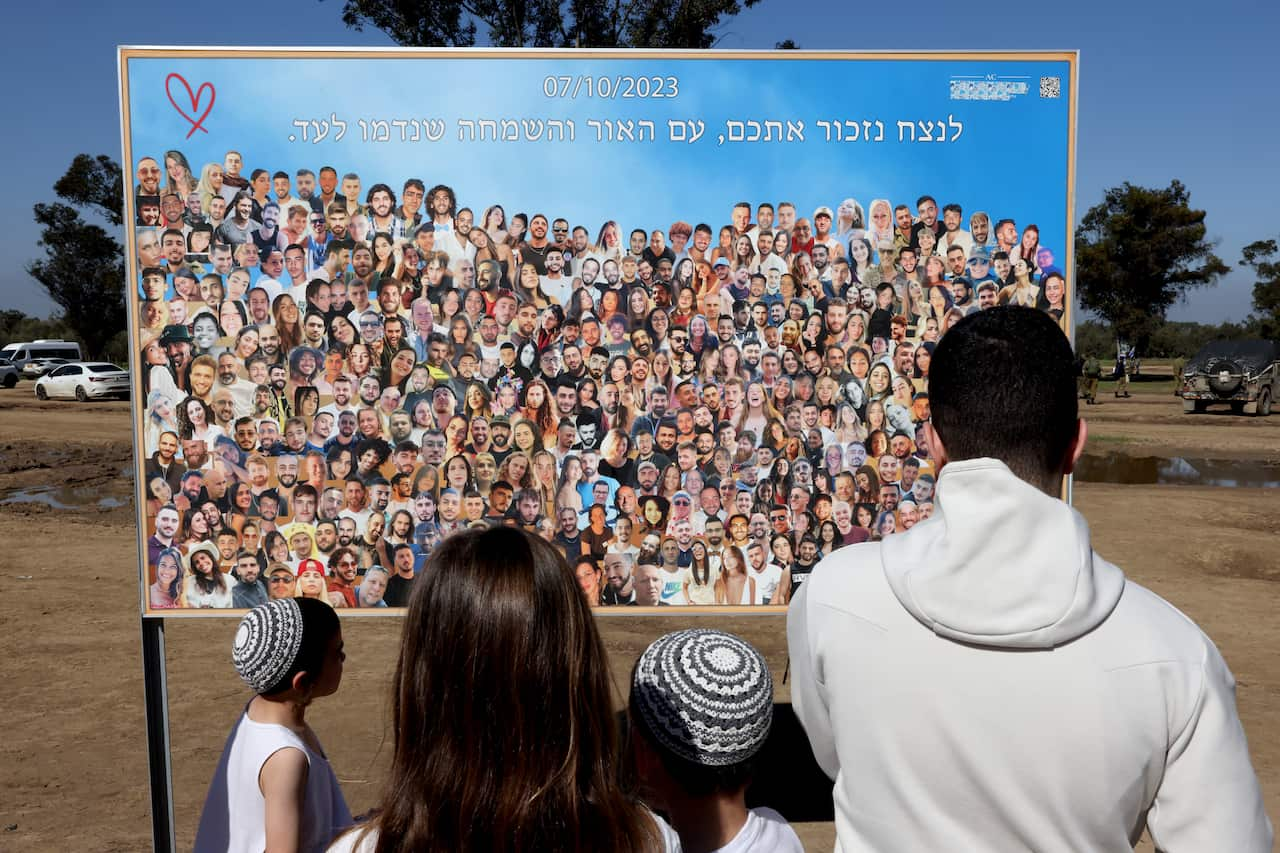 A family looks at a large sign with cut-out photos of hundreds of people.