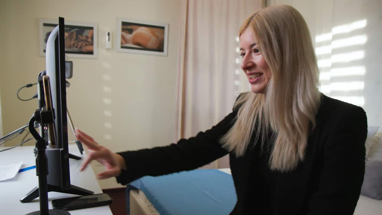 A blonde woman in a black blazer is talking in front of a mobile camera mounted on a tripod