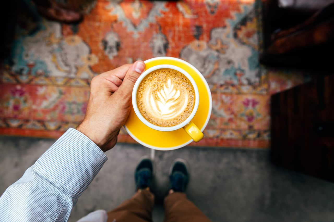Man holding yellow cup with cappuccino, personal perspective view.