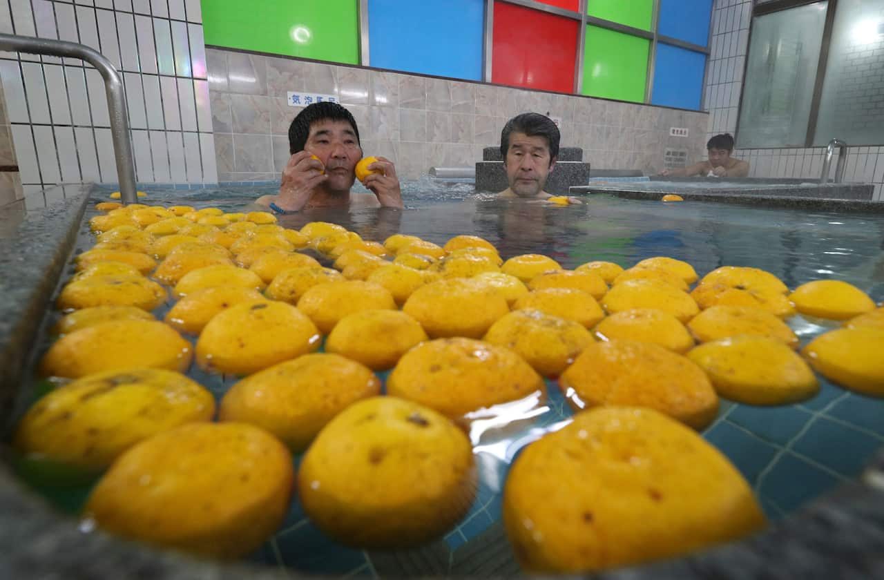 Two men sit in a spa filled with Yuzu fruit in a Japanese winter solstice tradition.