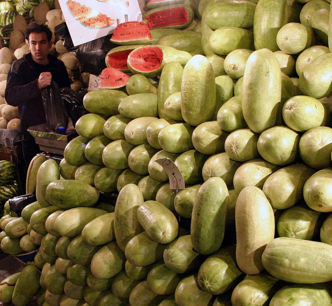 A man stands next to a large pile of watermelons for sale.