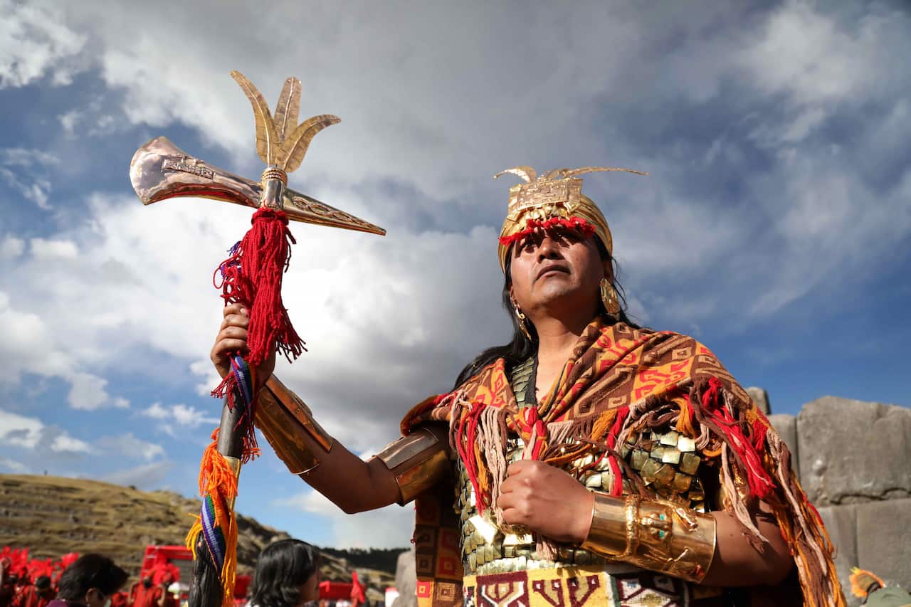 An artist in Peru dressed in traditional Inca clothing represents the sovereign of the Inca Empire in a recreation of the Inti Raymi celebration. He is pictured standing holding a traditional axe topped with feathers.
