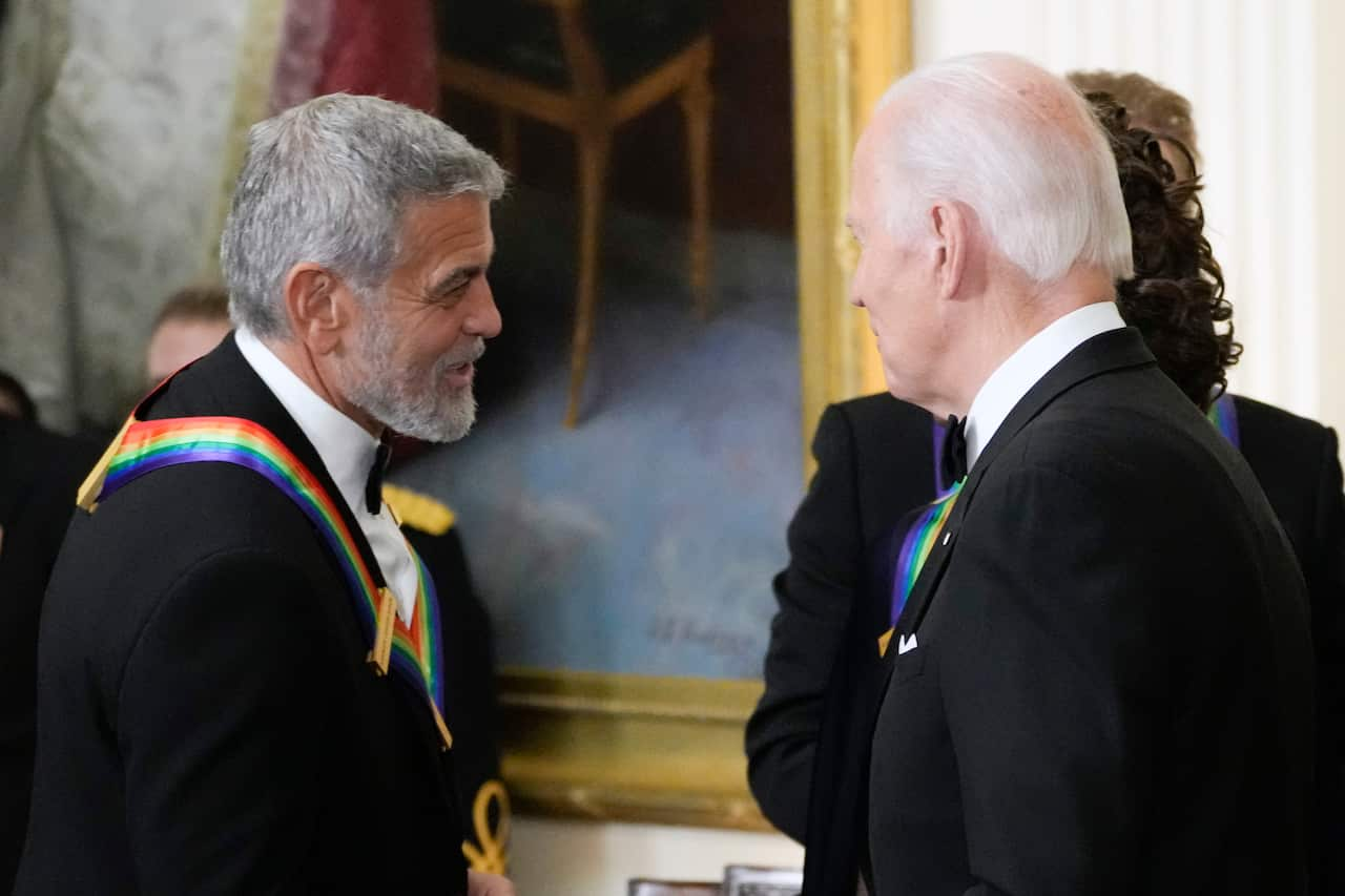 George Clooney and Joe Biden speaking to each other. They're both wearing suits and Clooney is wearing a ribbon sash.