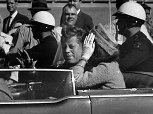 A black and white photograph of a man (former president John F Kennedy) and a woman (then first lady Jackie Onasis) riding in a convertible.