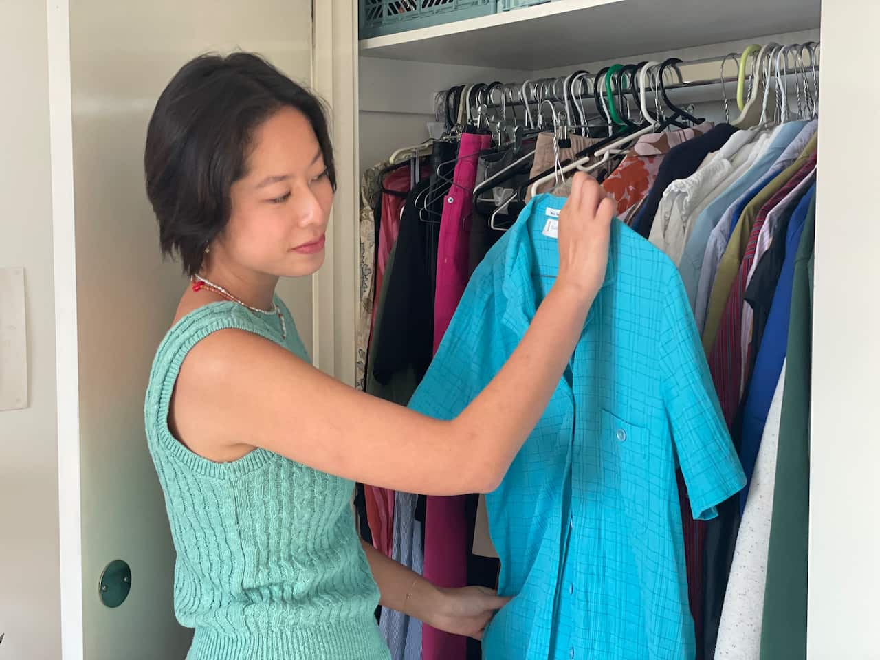 A woman taking a blue shirt out of a closet.