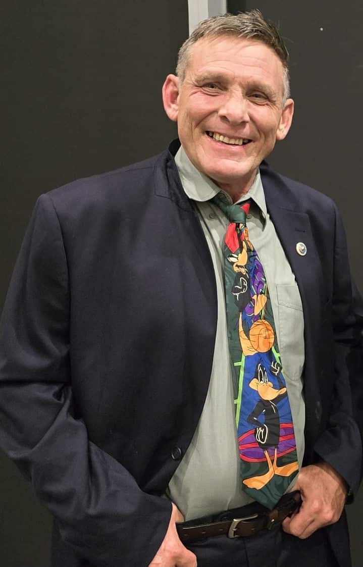 A man in a suit and colourful tie smiles at the camera.