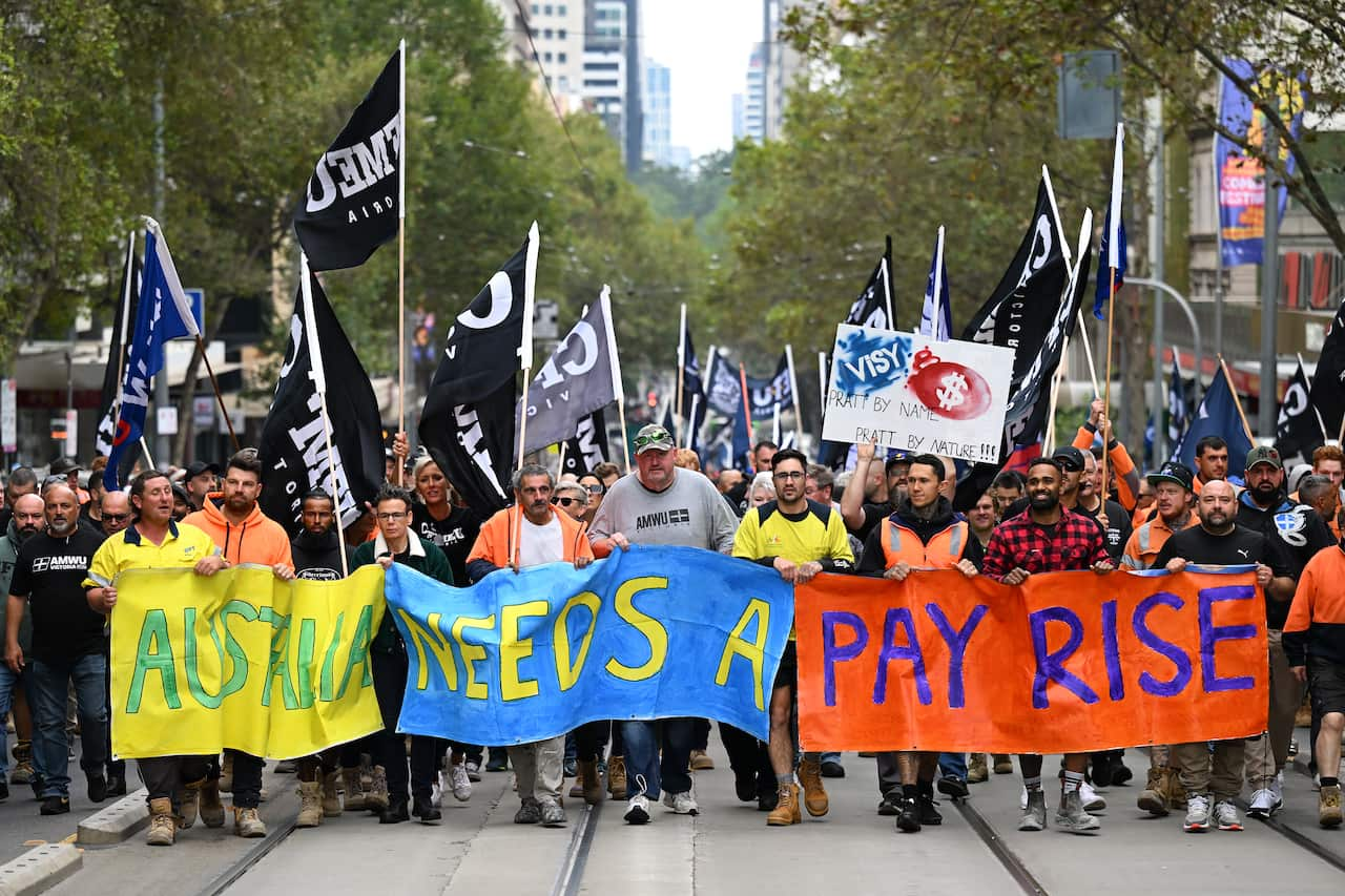 A group of men walking through Melbourne CBD, with a giant three part banner saying "Australia needs a payrise". Many are holding union flags as the protest.