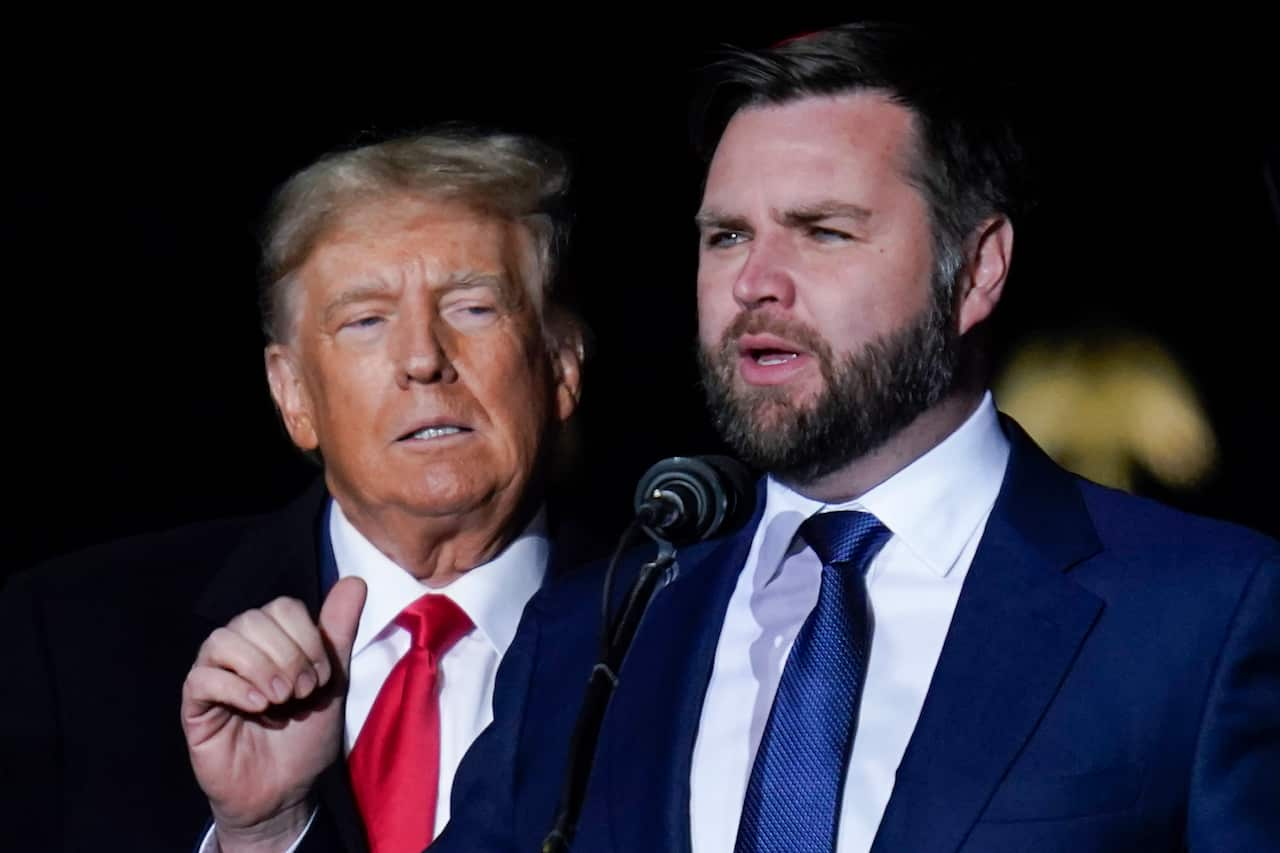 J.D. Vance speaking to a microphone with Donald Trump behind him. 