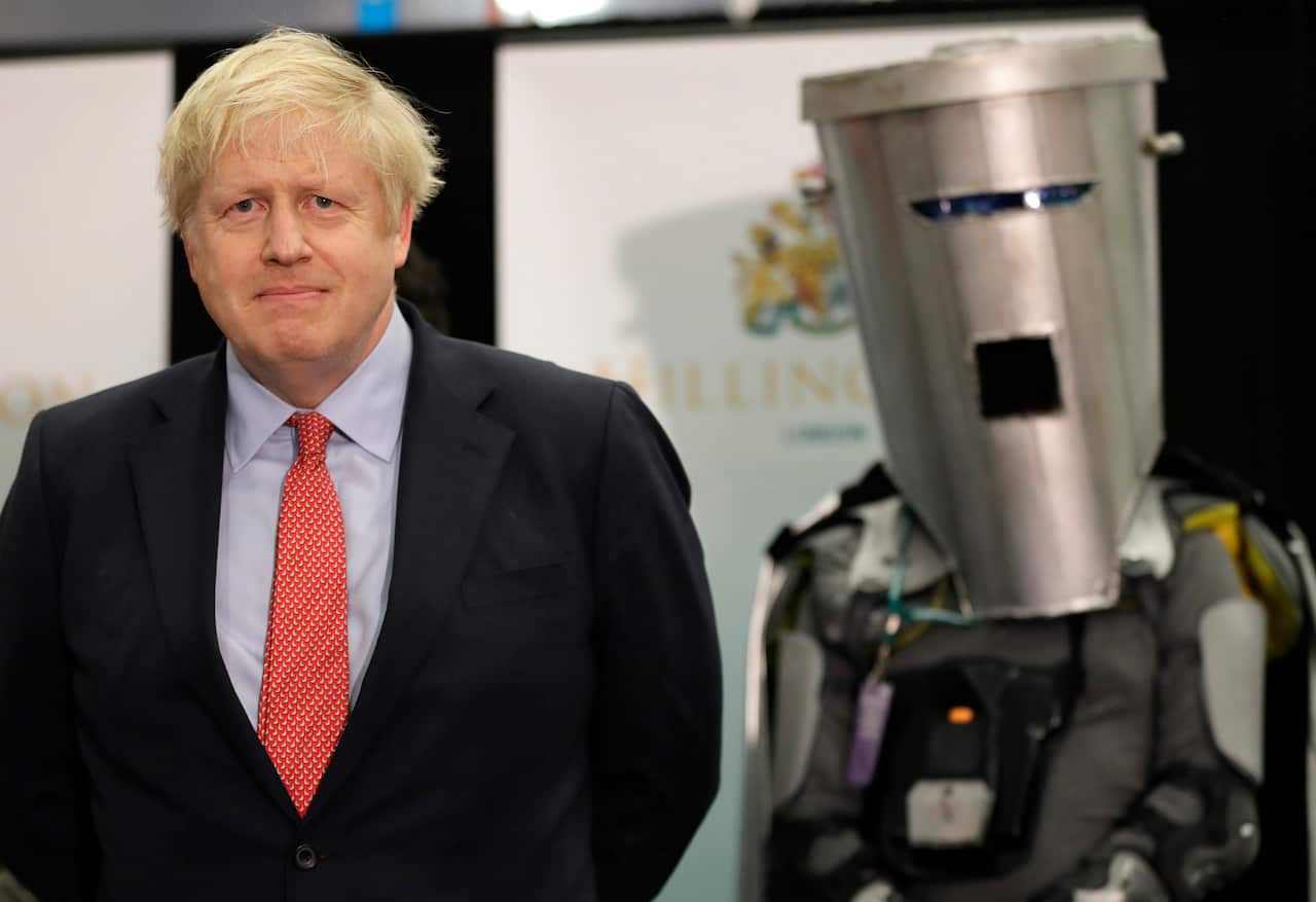 Former UK prime minister Boris Johnson stands next to a person in a grey costume that includes a bin on their head with slits for their eyes and mouth