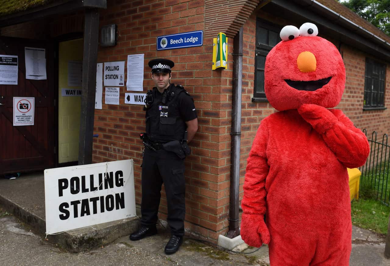 A man dressed in an Elmo suits stands outside a polling station as a police officer looks on