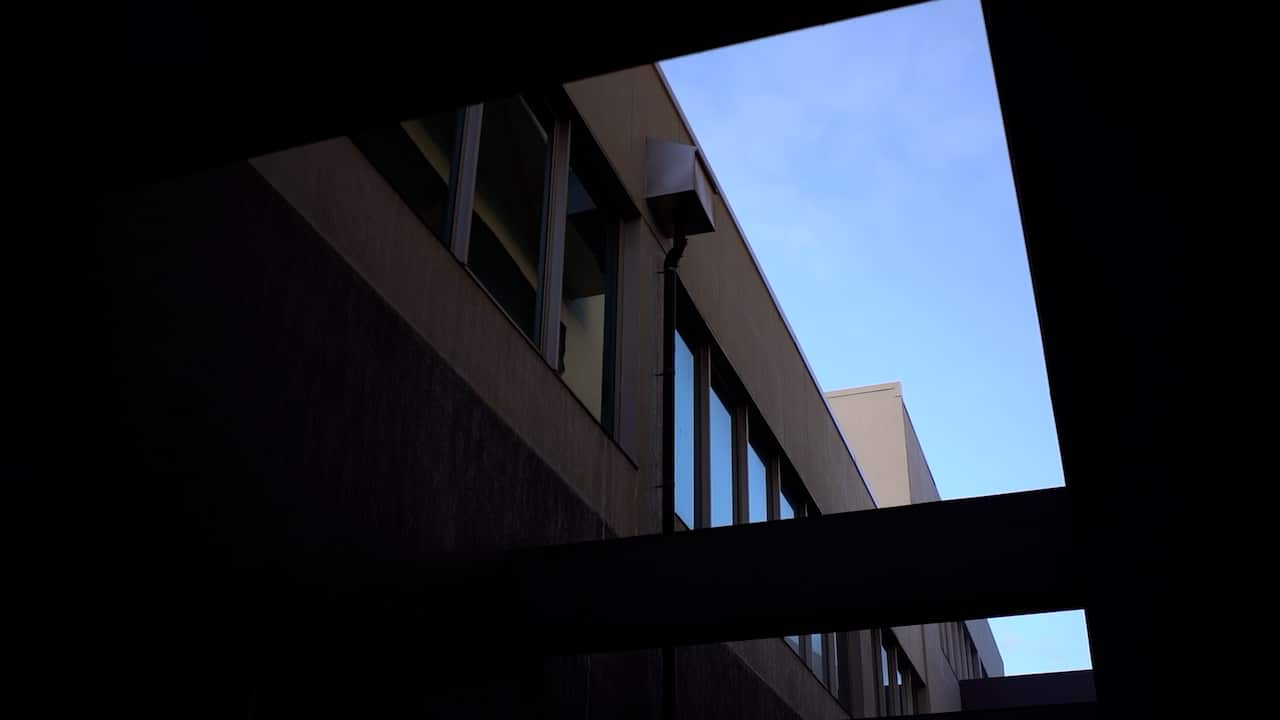 The ceiling window of a building shows a wall and blue sky above.