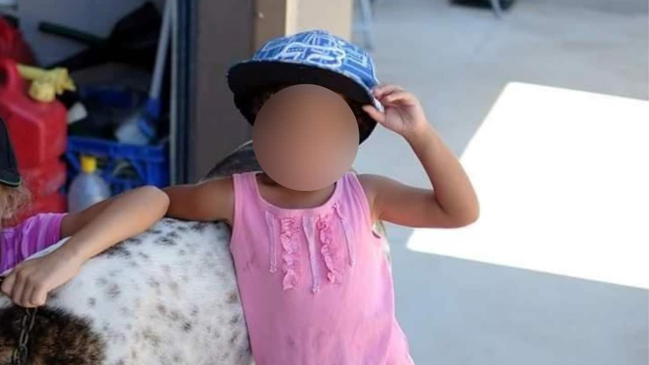 A child with a blurred face standing in a pink singlet. 