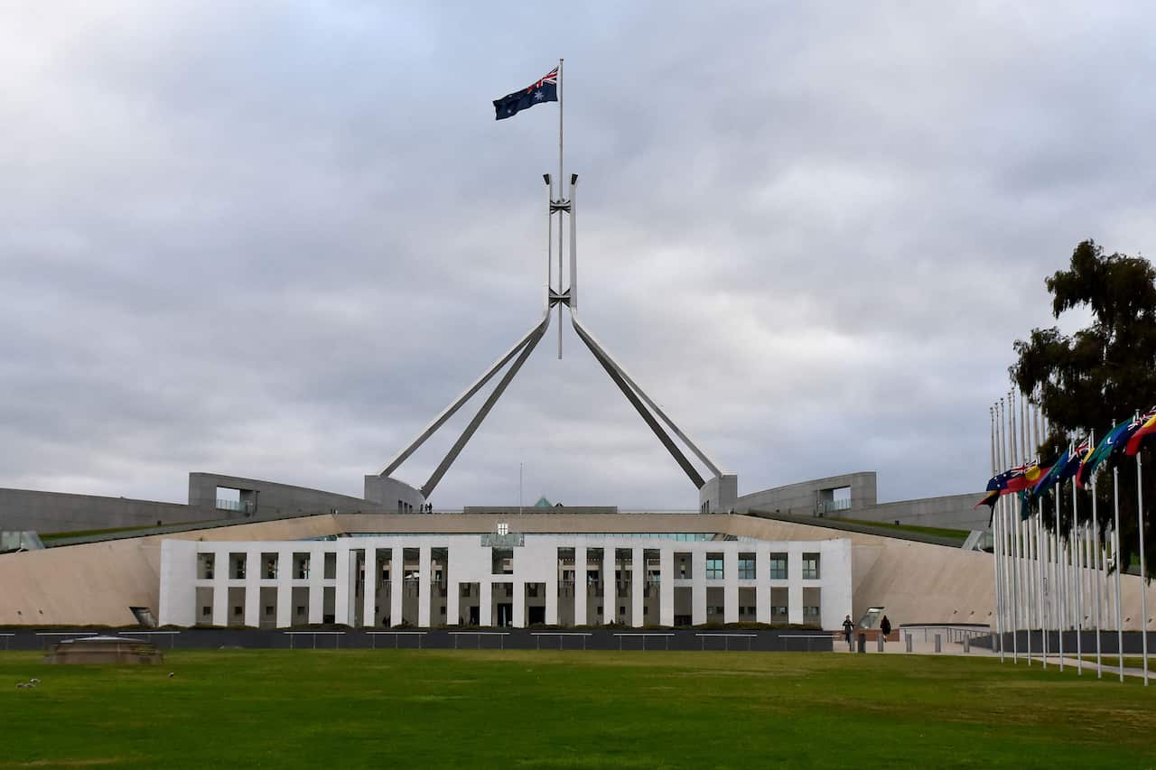 The Parliament House building on a cloudy day, with a green lawn in front of it.