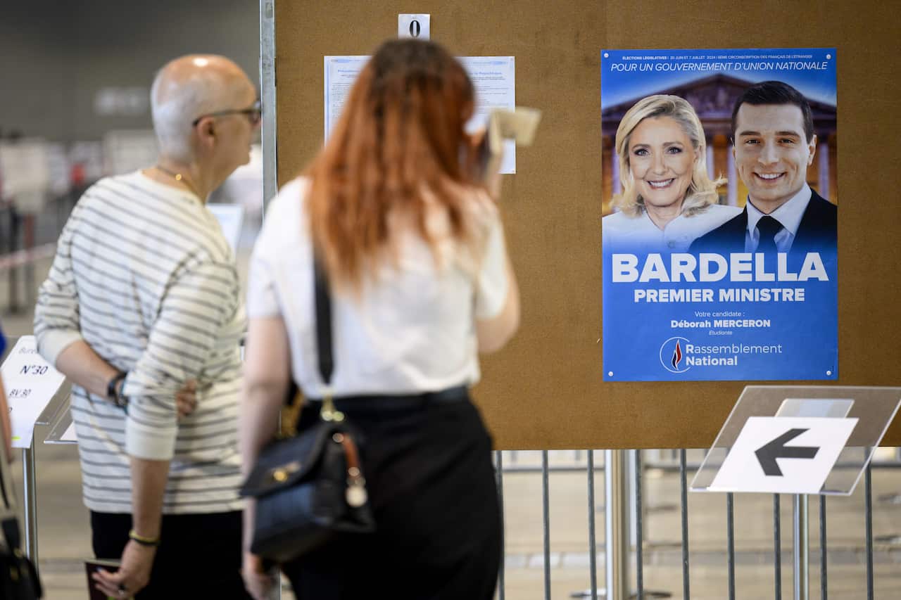 Two people look at a campaign poster featuring Marine Le Pen and Jordan Bardella