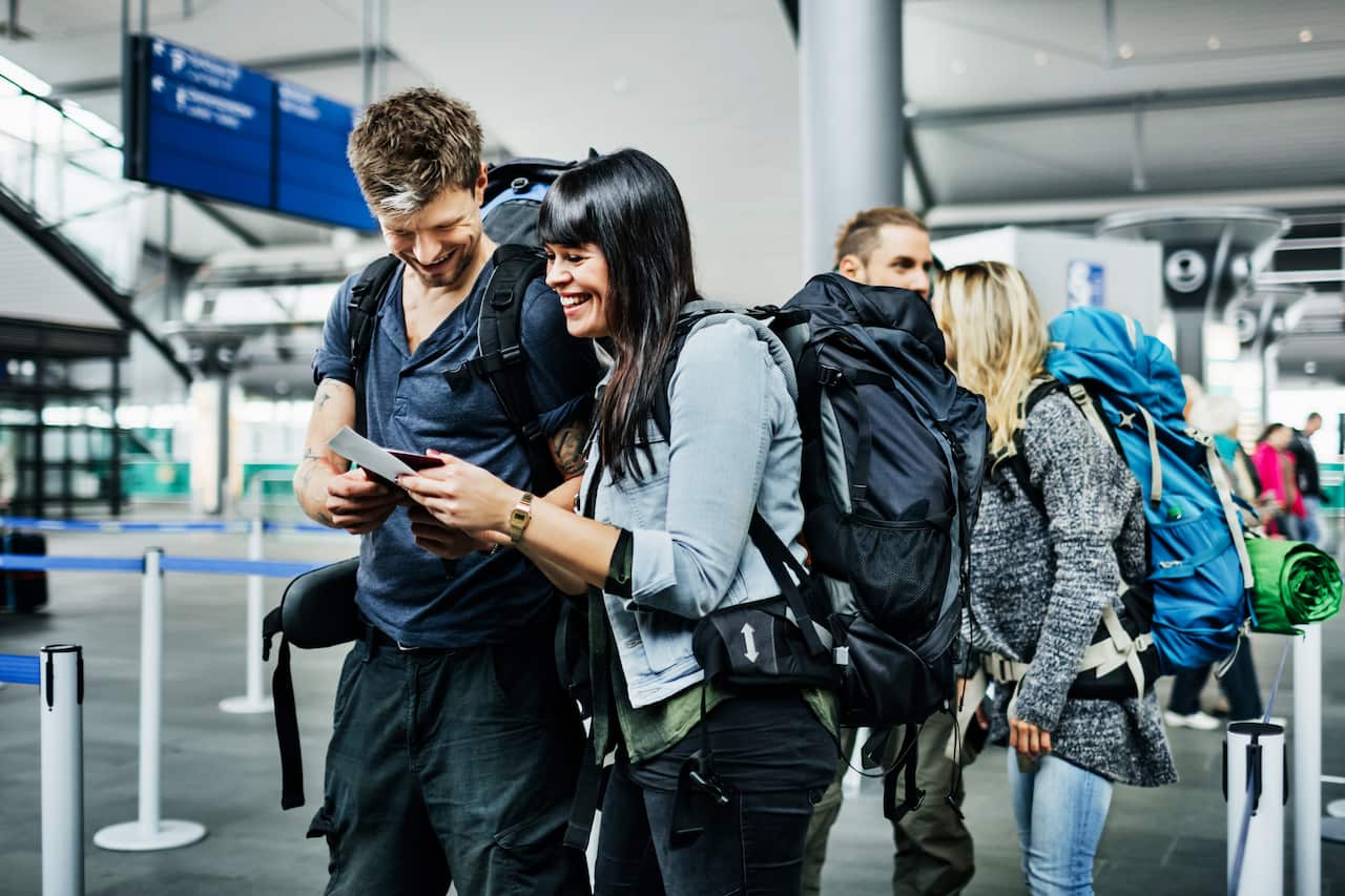Backpackers look at a smartphone while waiting near an airline check-in counter.