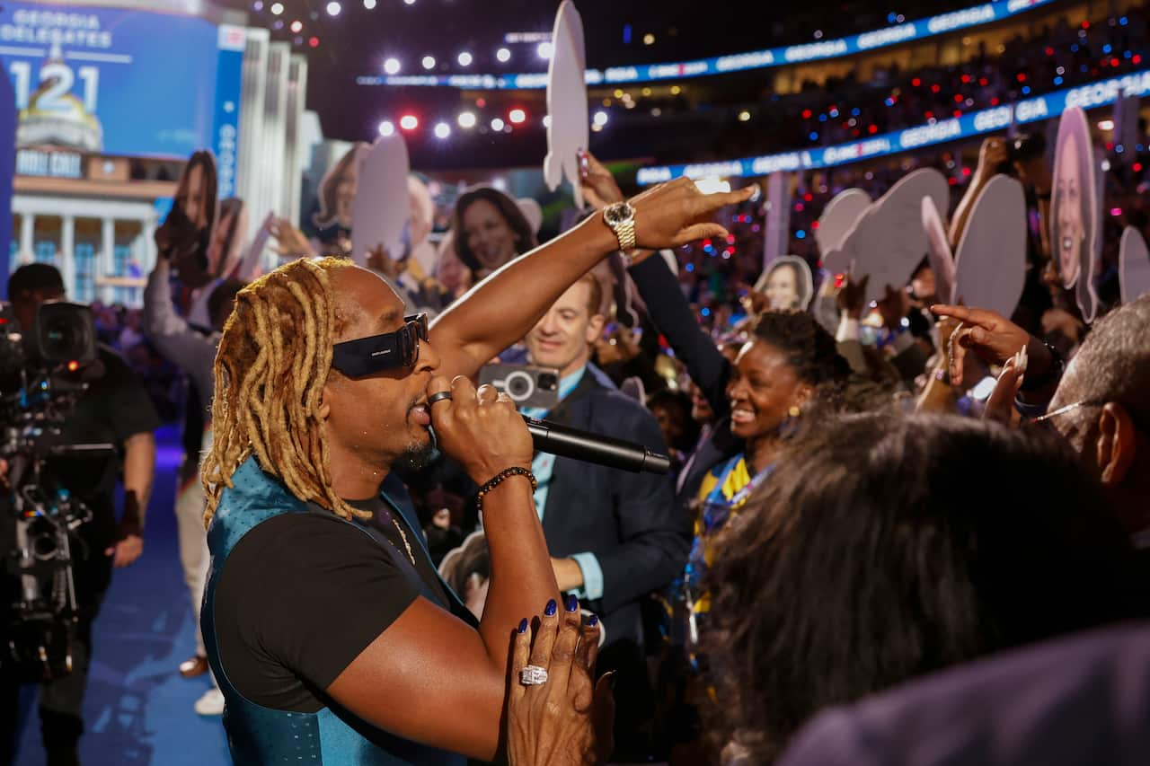 A man wearing sunnies is singing to a crowd of people