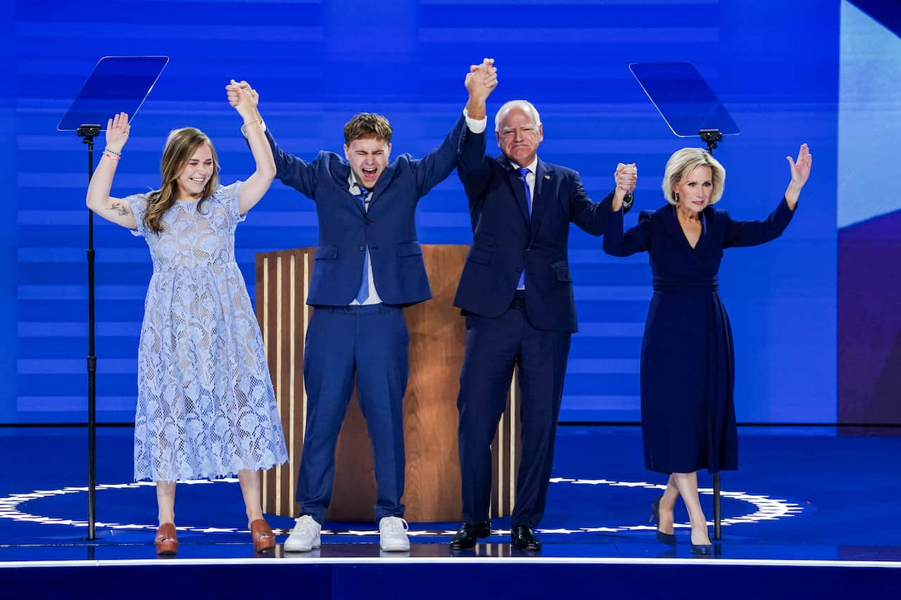 An older man, older woman, younger woman and younger man hold hands and put them up in celebration