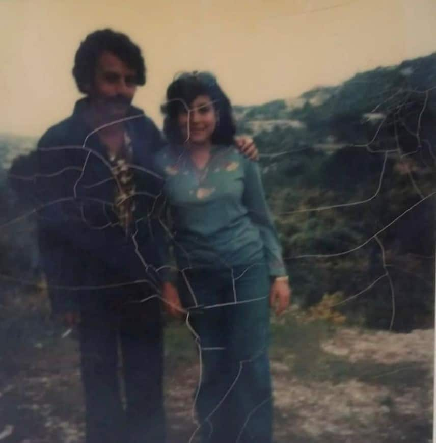 A man stands with his arm around a woman in cracked, old photo. 