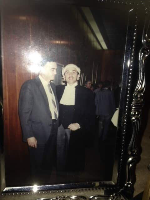 A man wearing a white barrister's wig poses with a man in a blue suit.