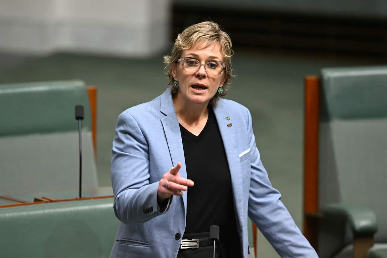 A woman in a blue suit points and she speaks.