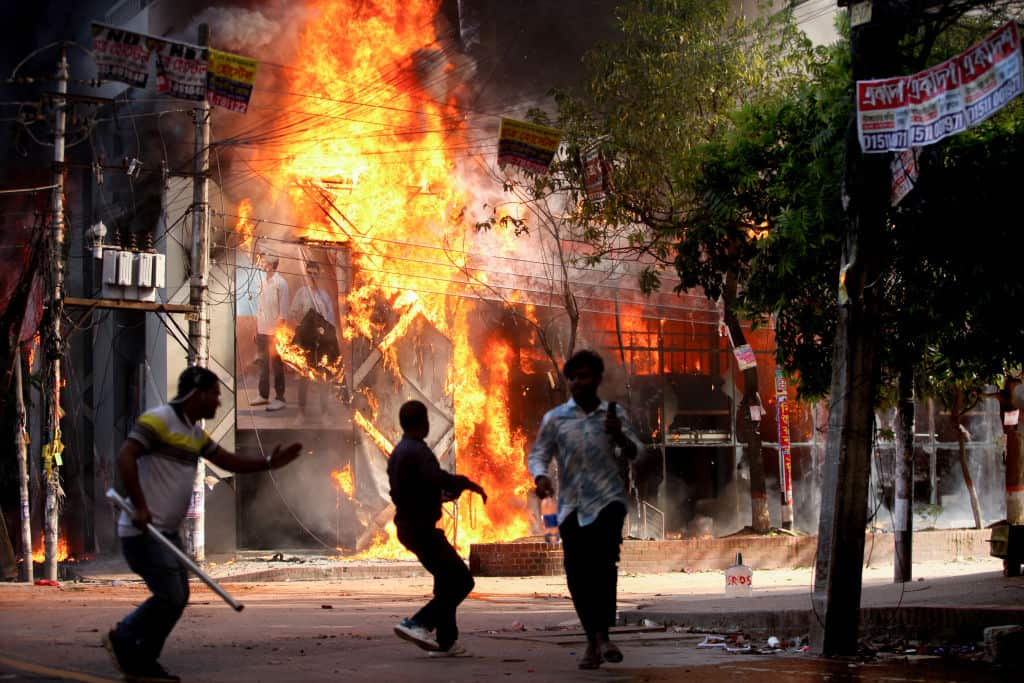 A building is on fire. Three men are in the foreground 