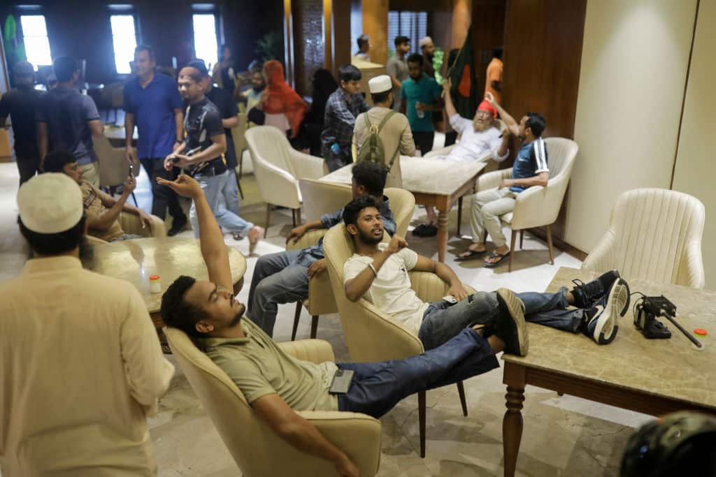 People in a large room. Some are sitting in chairs and others are standing.