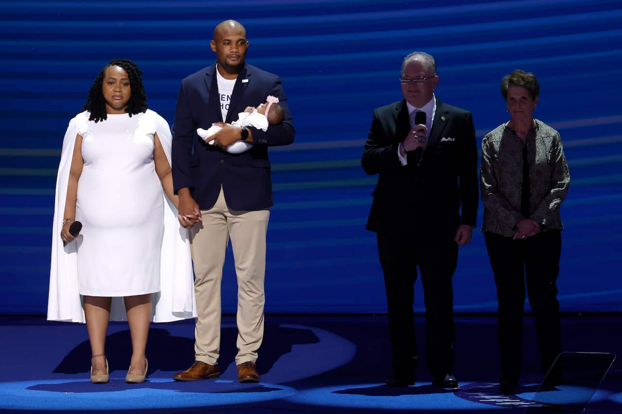 A couple and their baby under a spotlight on a stage, with another two people to one side of them.