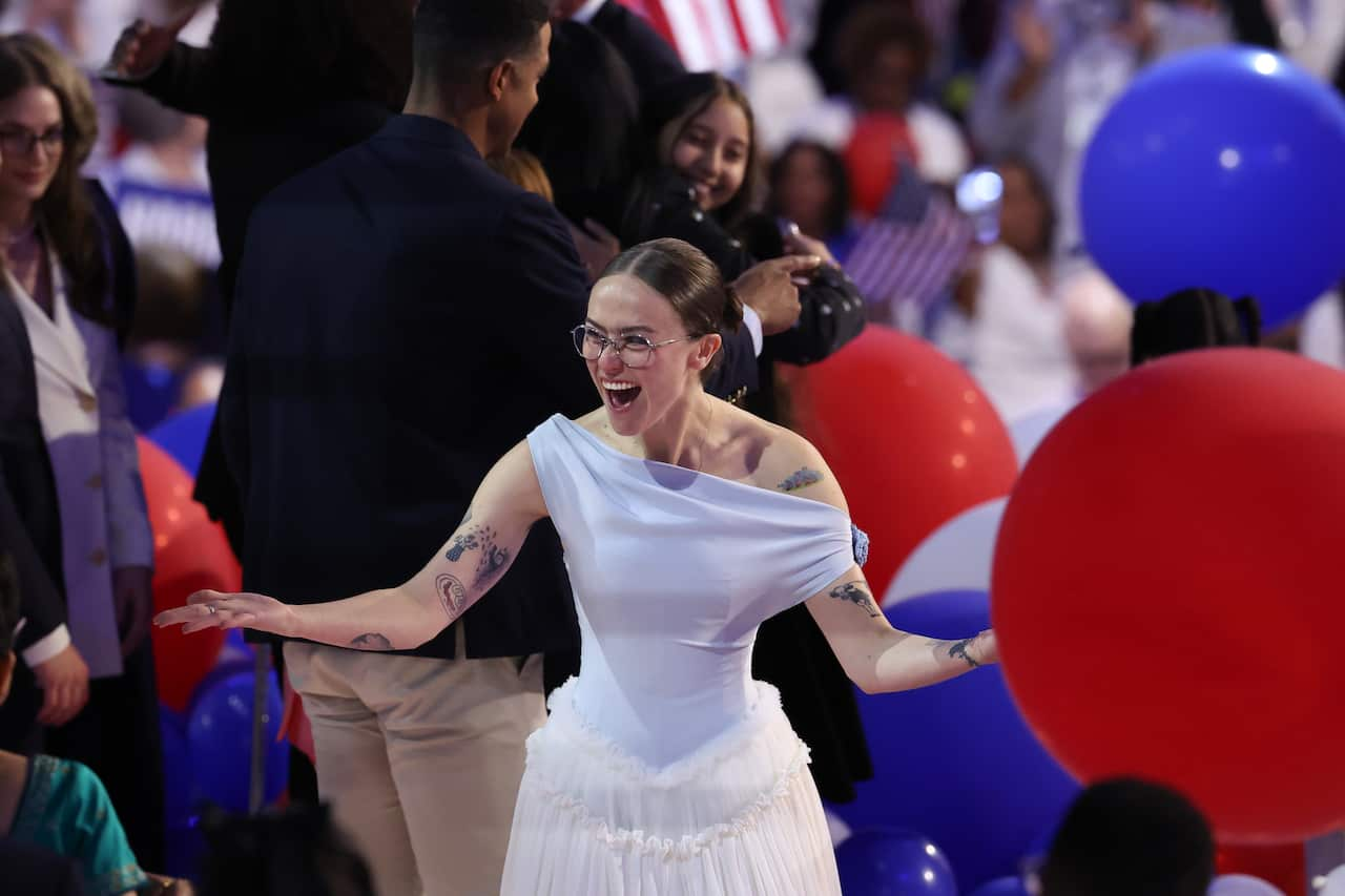 Ella Emhoff wearing a dress and glasses, celebrating among a crowd and balloons.