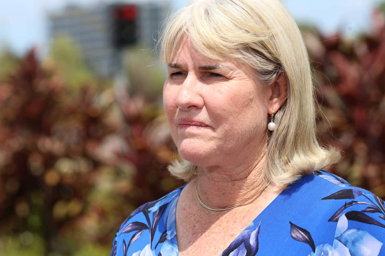 A blonde woman in a blue top looks forward with a serious expression on her face. 