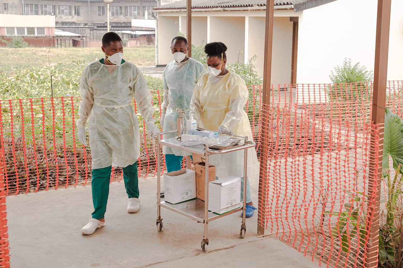 Three health workers wheel a cart 