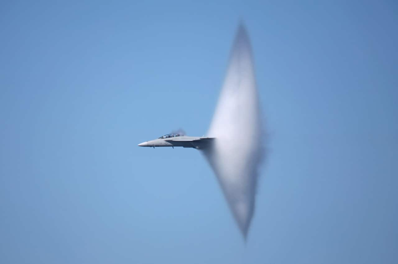 A fighter plane flies through a blue sky.