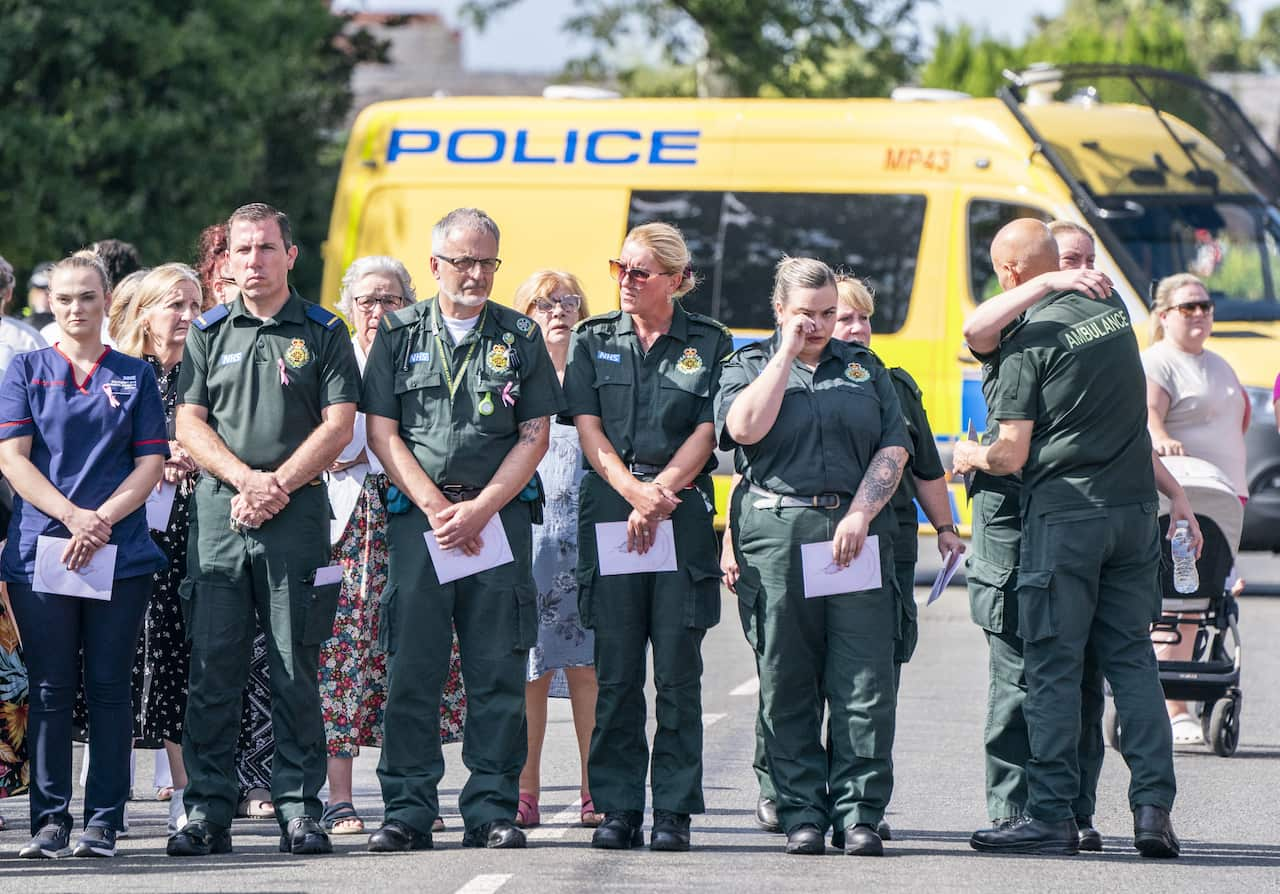 A line of people in green jumpsuits stand on a road 