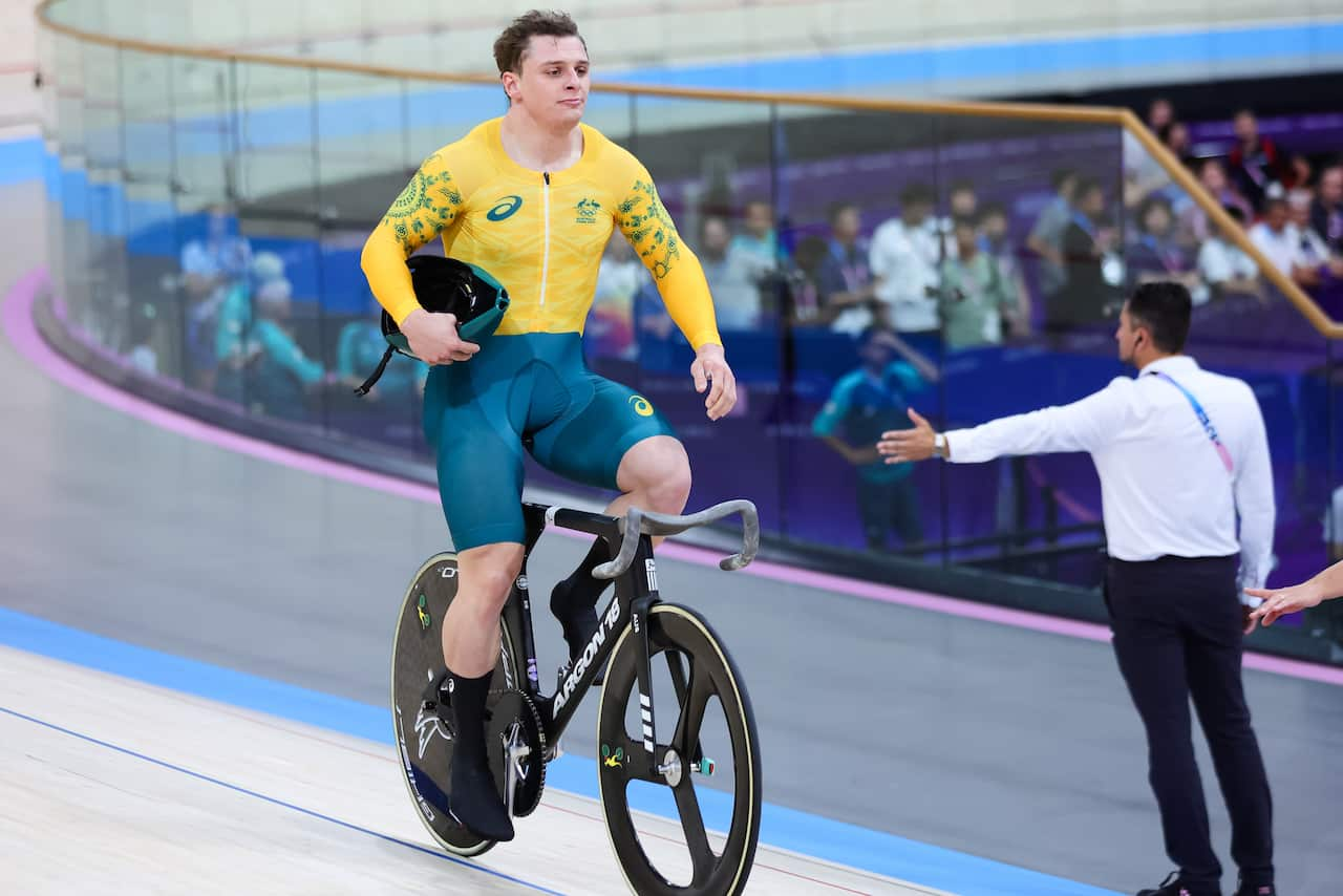 A man in a green and gold lycra outfit sits up on a bicycle