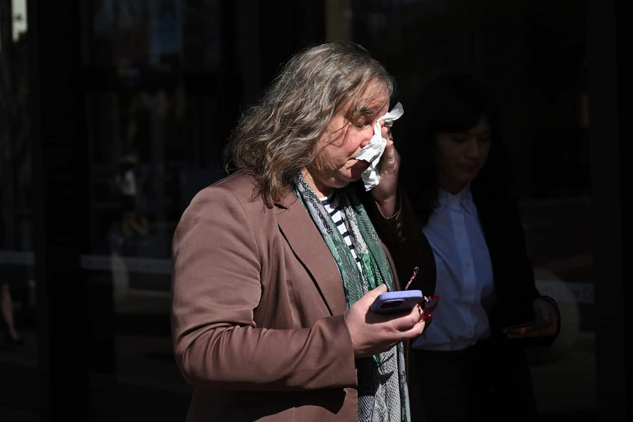 A woman wipes her eyes with a handkerchied as she walks outside.