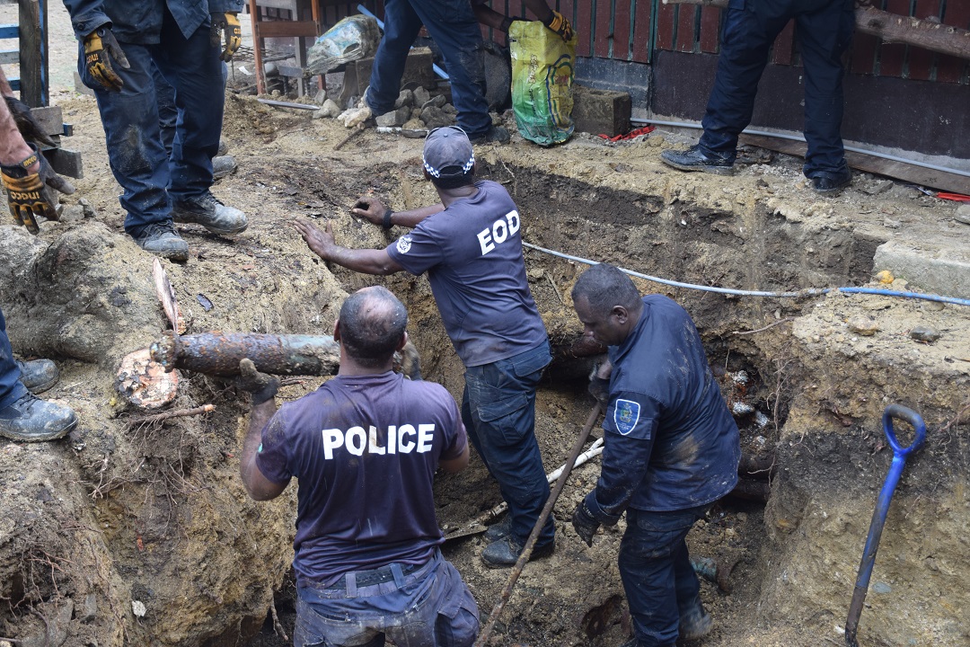 Officers in a 1.5m deep hole pass a long rusty bomb to officers above them.