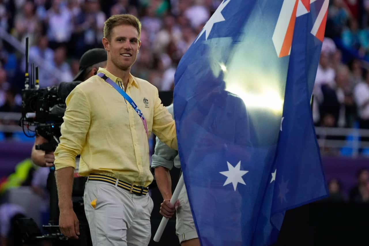 A man wearing a yellow shirt and light coloured long pants carrying an Australian flag  